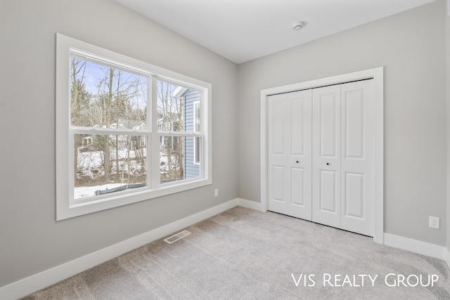 unfurnished bedroom featuring a closet, light colored carpet, visible vents, and baseboards
