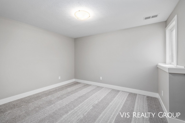 carpeted spare room with a textured ceiling, visible vents, and baseboards