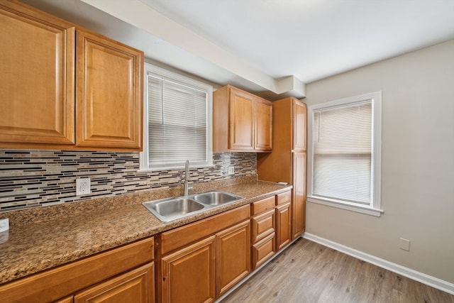 kitchen with tasteful backsplash, stone countertops, sink, and light wood-type flooring