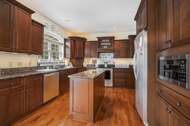 kitchen with stainless steel appliances, hardwood / wood-style flooring, a center island, and dark stone counters