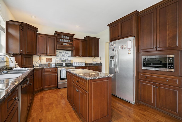 kitchen featuring sink, dark stone countertops, appliances with stainless steel finishes, a kitchen island, and hardwood / wood-style floors