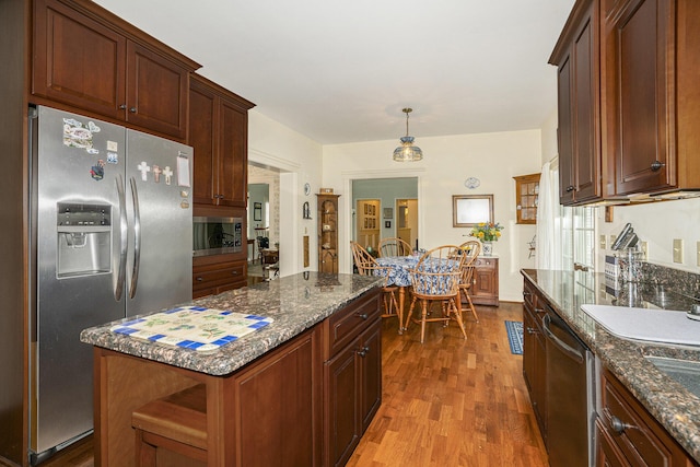 kitchen featuring pendant lighting, stainless steel appliances, a kitchen island, dark stone counters, and light wood-type flooring