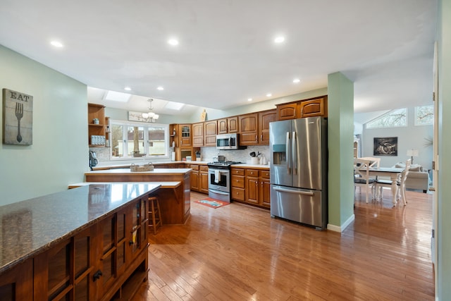 kitchen with tasteful backsplash, light wood-type flooring, dark stone counters, and appliances with stainless steel finishes