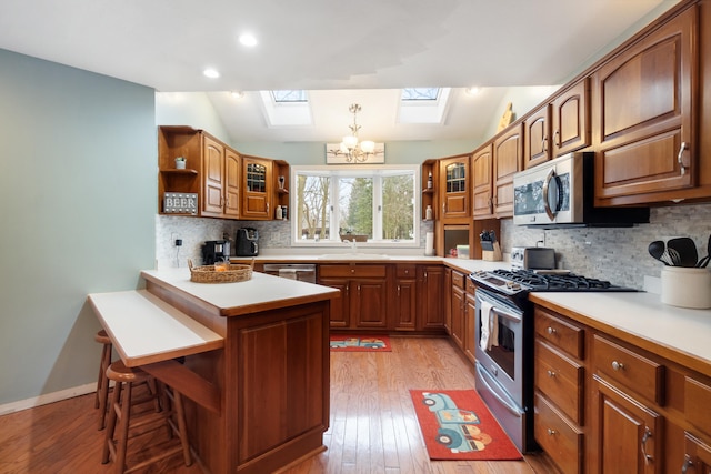 kitchen featuring lofted ceiling with skylight, appliances with stainless steel finishes, a breakfast bar, decorative backsplash, and light wood-type flooring