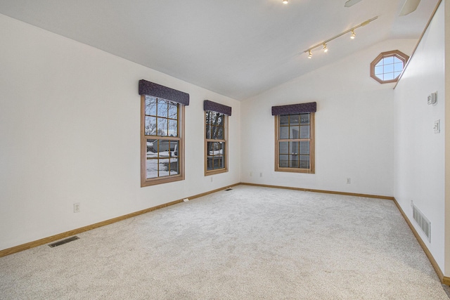 unfurnished room featuring rail lighting, lofted ceiling, plenty of natural light, and light colored carpet