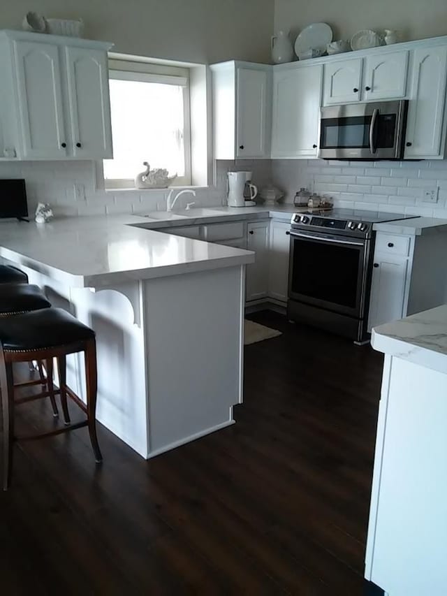 kitchen with a breakfast bar, backsplash, stainless steel appliances, white cabinets, and dark hardwood / wood-style flooring