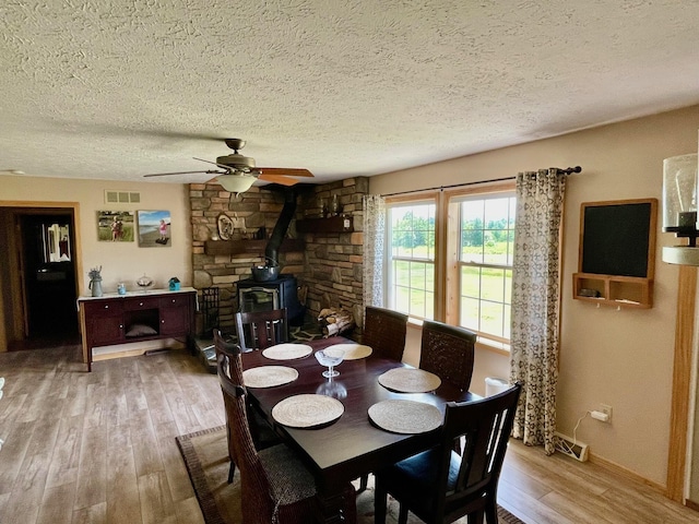 dining room featuring ceiling fan, hardwood / wood-style floors, a textured ceiling, and a wood stove