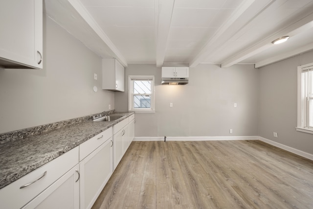 kitchen featuring beam ceiling, white cabinetry, light wood-type flooring, and light stone counters