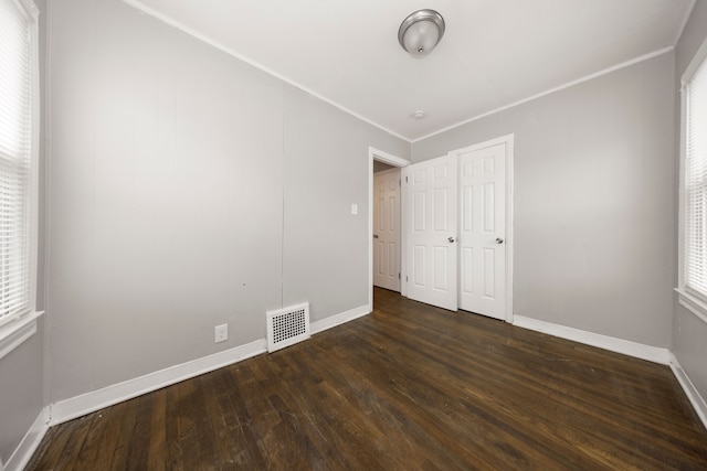 unfurnished bedroom with dark hardwood / wood-style flooring, multiple windows, ornamental molding, and a closet