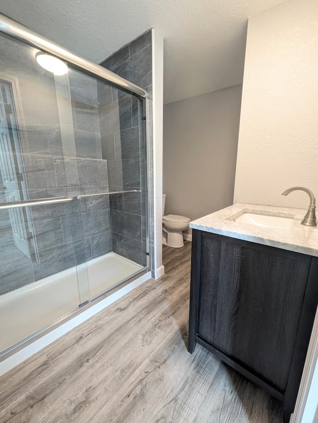 bathroom featuring a shower with door, vanity, wood-type flooring, a textured ceiling, and toilet