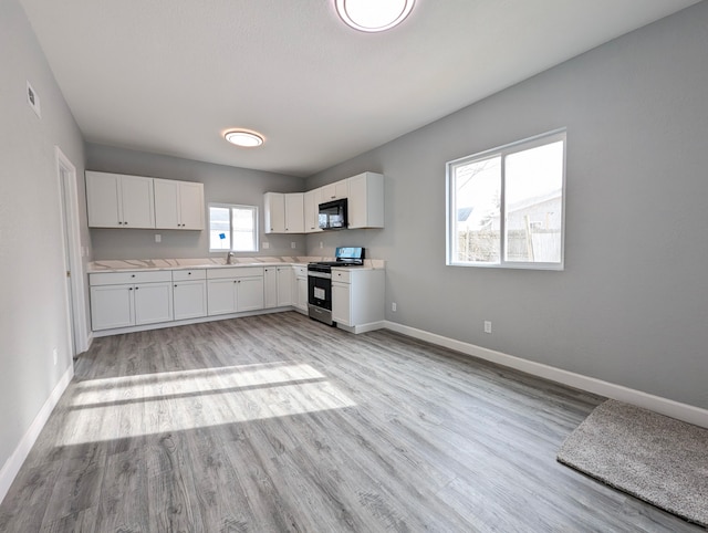 kitchen with sink, stainless steel gas range oven, light hardwood / wood-style floors, and white cabinets