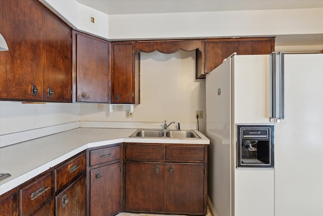 kitchen featuring dark brown cabinets, white fridge with ice dispenser, and sink