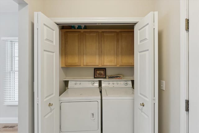 clothes washing area featuring cabinets, a healthy amount of sunlight, and washing machine and clothes dryer