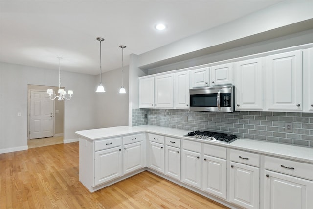 kitchen with appliances with stainless steel finishes, pendant lighting, white cabinetry, light hardwood / wood-style floors, and kitchen peninsula