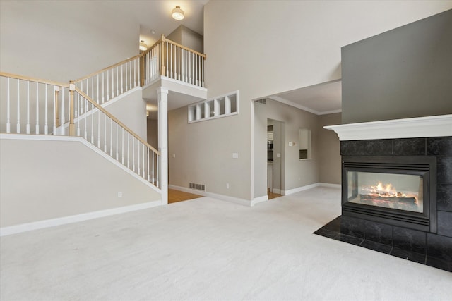 unfurnished living room featuring ornamental molding, a tiled fireplace, carpet floors, and a high ceiling