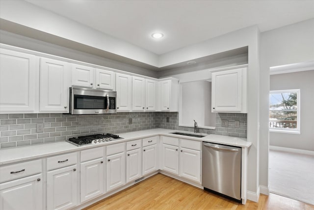 kitchen with appliances with stainless steel finishes, sink, white cabinets, and light hardwood / wood-style floors