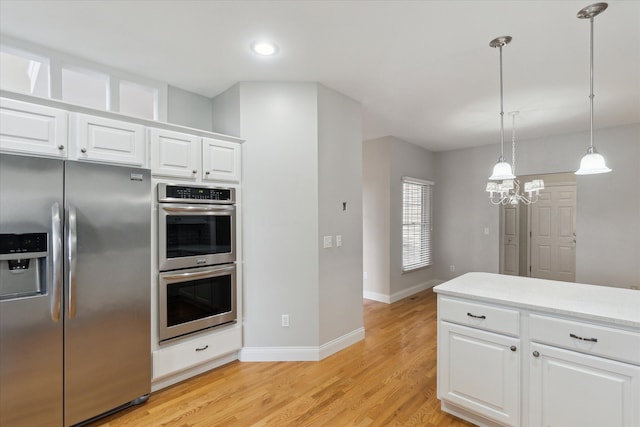 kitchen with white cabinetry, hanging light fixtures, stainless steel appliances, and light wood-type flooring