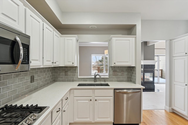 kitchen with sink, white cabinetry, light wood-type flooring, stainless steel appliances, and decorative backsplash