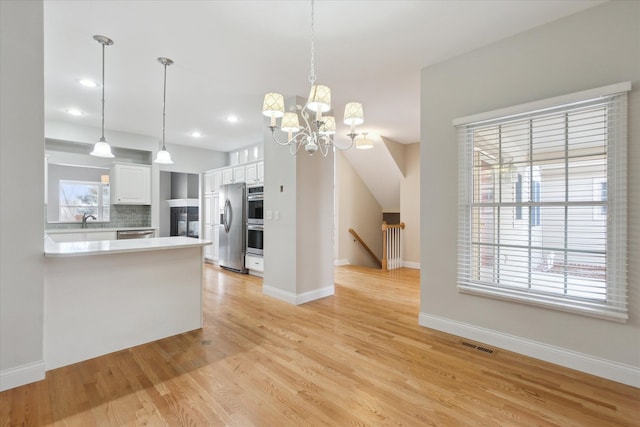 kitchen with white cabinetry, stainless steel appliances, light hardwood / wood-style floors, and hanging light fixtures