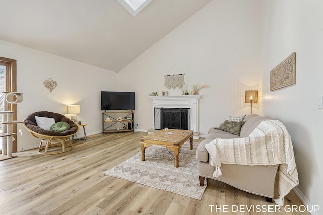 living room with high vaulted ceiling, a skylight, and light hardwood / wood-style floors