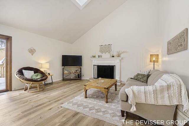 living room featuring a skylight, high vaulted ceiling, and light wood-type flooring