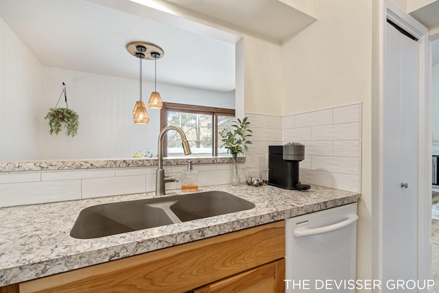 kitchen with sink, tasteful backsplash, light stone counters, decorative light fixtures, and dishwasher