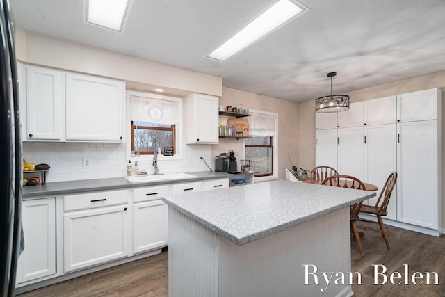 kitchen with pendant lighting, sink, dark wood-type flooring, white cabinetry, and a center island