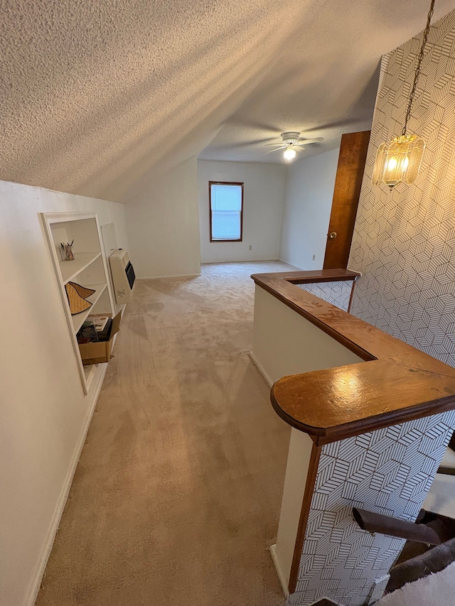 hall featuring lofted ceiling, light colored carpet, and a textured ceiling