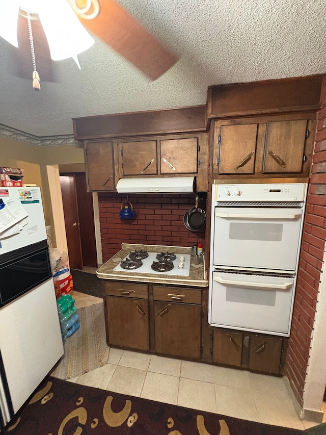 kitchen featuring light tile patterned flooring, brick wall, white appliances, dark brown cabinetry, and a textured ceiling