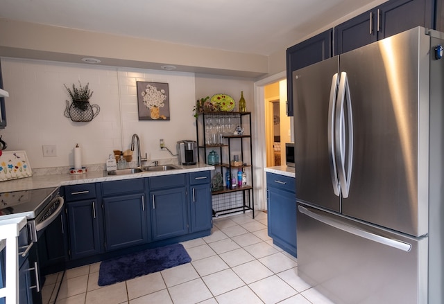 kitchen featuring blue cabinets, sink, light tile patterned floors, stainless steel refrigerator, and range with electric cooktop