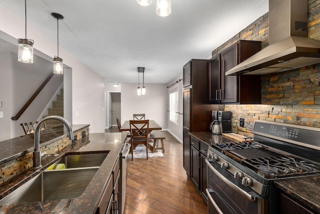 kitchen featuring hanging light fixtures, appliances with stainless steel finishes, dark stone counters, and wall chimney exhaust hood