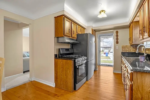 kitchen featuring sink, dark stone countertops, decorative backsplash, light hardwood / wood-style floors, and stainless steel gas range