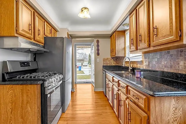 kitchen with tasteful backsplash, appliances with stainless steel finishes, dark stone countertops, and light wood-type flooring