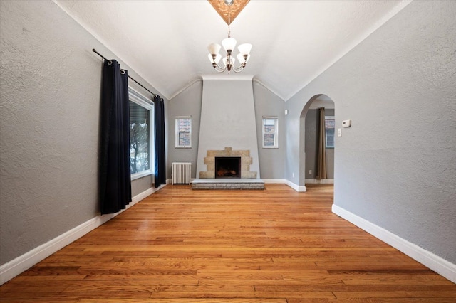 unfurnished living room featuring light hardwood / wood-style flooring, radiator heating unit, a notable chandelier, a stone fireplace, and vaulted ceiling