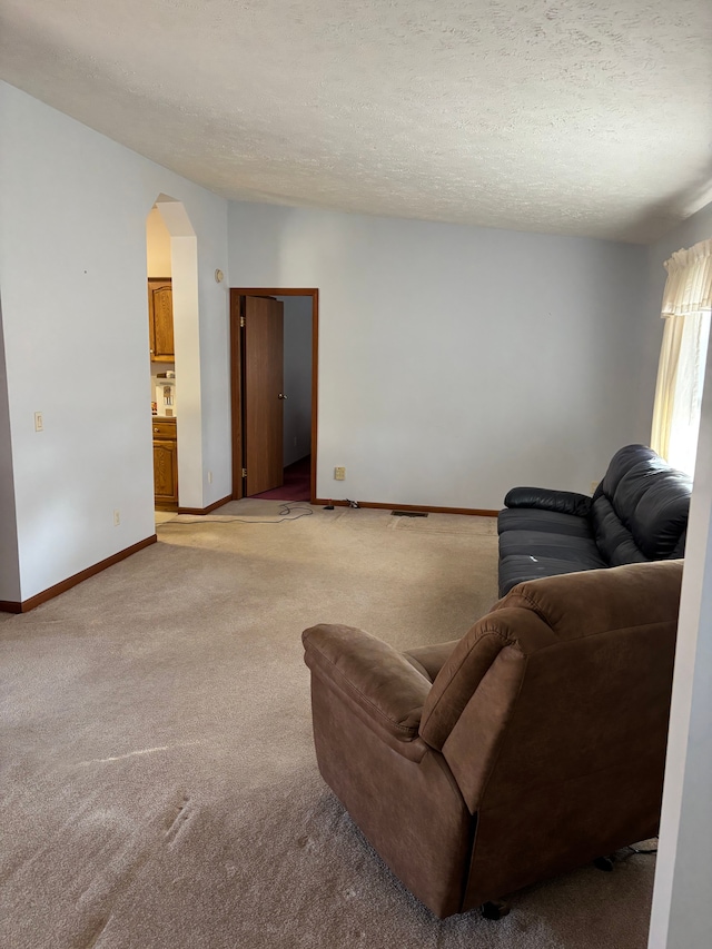 living area featuring baseboards, arched walkways, a textured ceiling, and light colored carpet