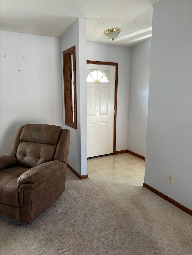 foyer entrance featuring baseboards, a textured ceiling, and light colored carpet