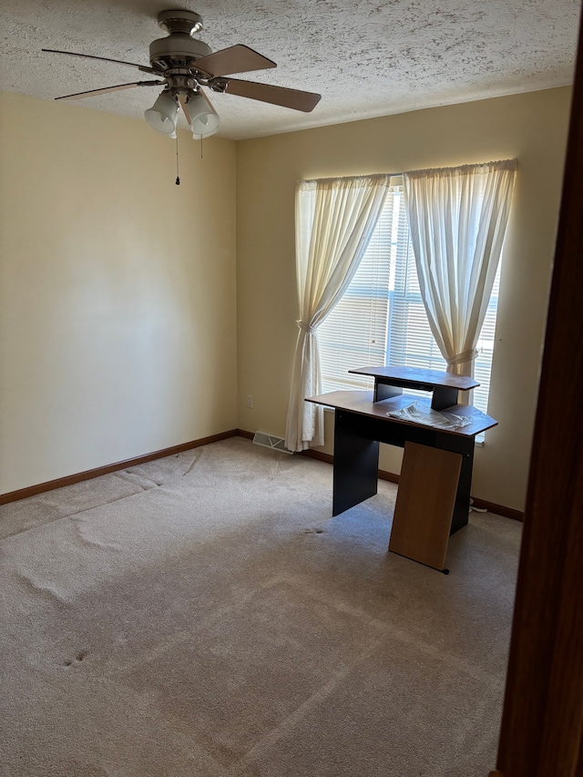 unfurnished office with a textured ceiling, light colored carpet, a ceiling fan, baseboards, and visible vents