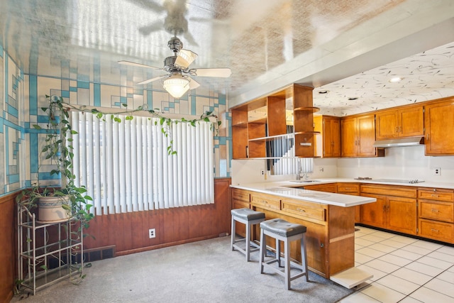 kitchen featuring ceiling fan, a kitchen bar, light tile patterned flooring, black electric cooktop, and kitchen peninsula