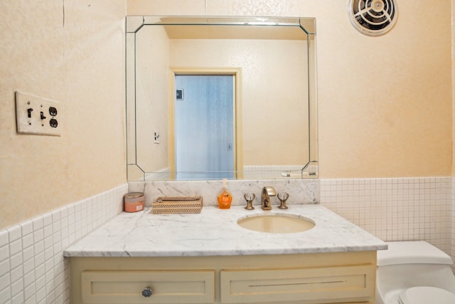 bathroom with vanity, toilet, and tile walls