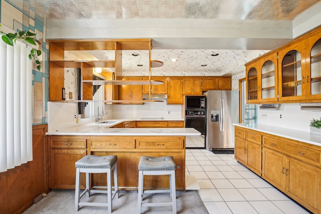 kitchen with sink, light tile patterned floors, black appliances, a kitchen bar, and kitchen peninsula