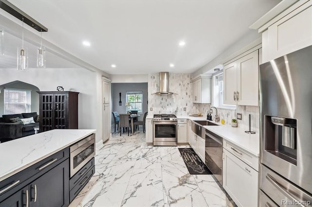 kitchen with pendant lighting, wall chimney range hood, white cabinetry, and stainless steel appliances