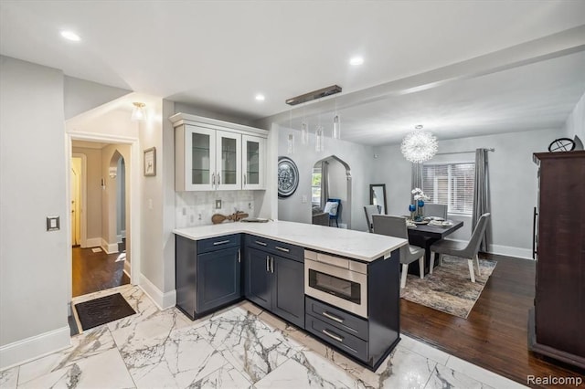 kitchen featuring pendant lighting, stainless steel microwave, white cabinets, backsplash, and kitchen peninsula