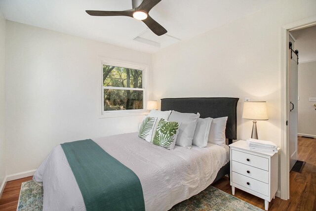 bedroom featuring a barn door, dark wood-type flooring, and ceiling fan