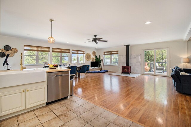 kitchen featuring sink, decorative light fixtures, a wood stove, light wood-type flooring, and dishwasher