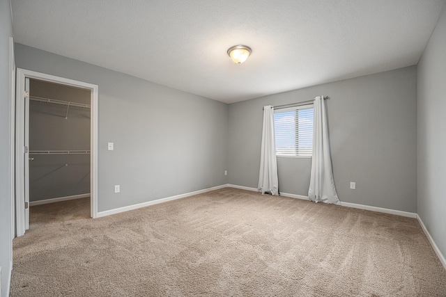 unfurnished bedroom with a closet, a spacious closet, light carpet, and a textured ceiling