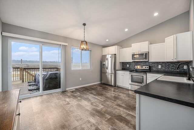 kitchen with appliances with stainless steel finishes, decorative light fixtures, lofted ceiling, sink, and white cabinets