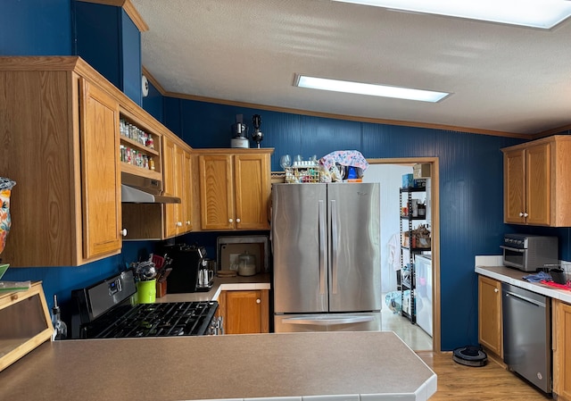 kitchen with ornamental molding, kitchen peninsula, stainless steel appliances, a textured ceiling, and light hardwood / wood-style flooring