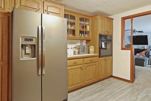 kitchen with black oven, stainless steel fridge, light hardwood / wood-style floors, ceiling fan, and a textured ceiling