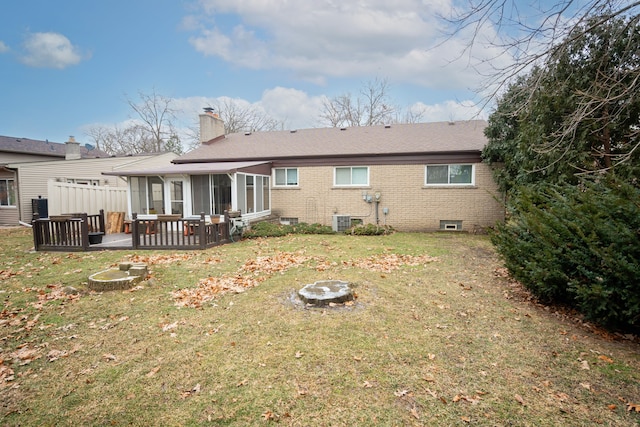 rear view of property featuring a fire pit, a wooden deck, a yard, central air condition unit, and a sunroom