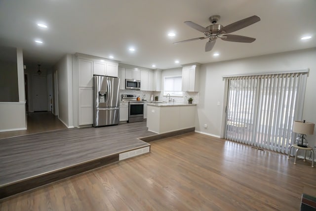 kitchen with ceiling fan, stainless steel appliances, hardwood / wood-style floors, decorative backsplash, and white cabinets